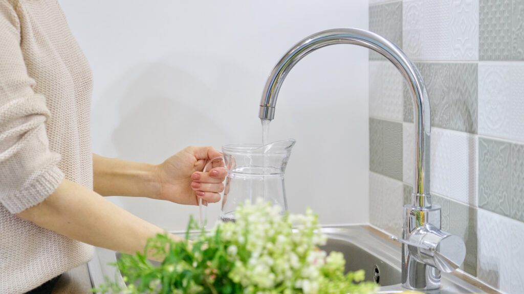 Clean water pouring from kitchen sink faucet into pitcher
