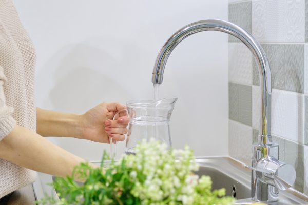 Clean water pouring from kitchen sink faucet into pitcher
